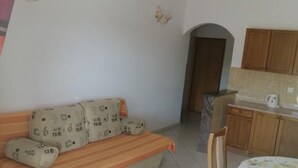 A room with a sofa, a small table, wooden cabinets, and a kitchen area.