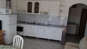 A compact kitchen with white cabinets, a microwave, a stove, and a sink. There is a dining table with chairs and a sofa in the living area. - Apartments Milakovic-Kanica - One Bedroom Apartment with Sea View and Terrace (Rogoznica)