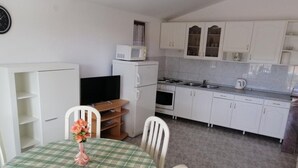 A compact kitchen with white cabinets, a microwave, a stove, and a sink. There is a dining table with a plaid tablecloth and a vase with flowers. - Apartments Milakovic-Kanica - One Bedroom Apartment with Sea View and Terrace (Rogoznica)