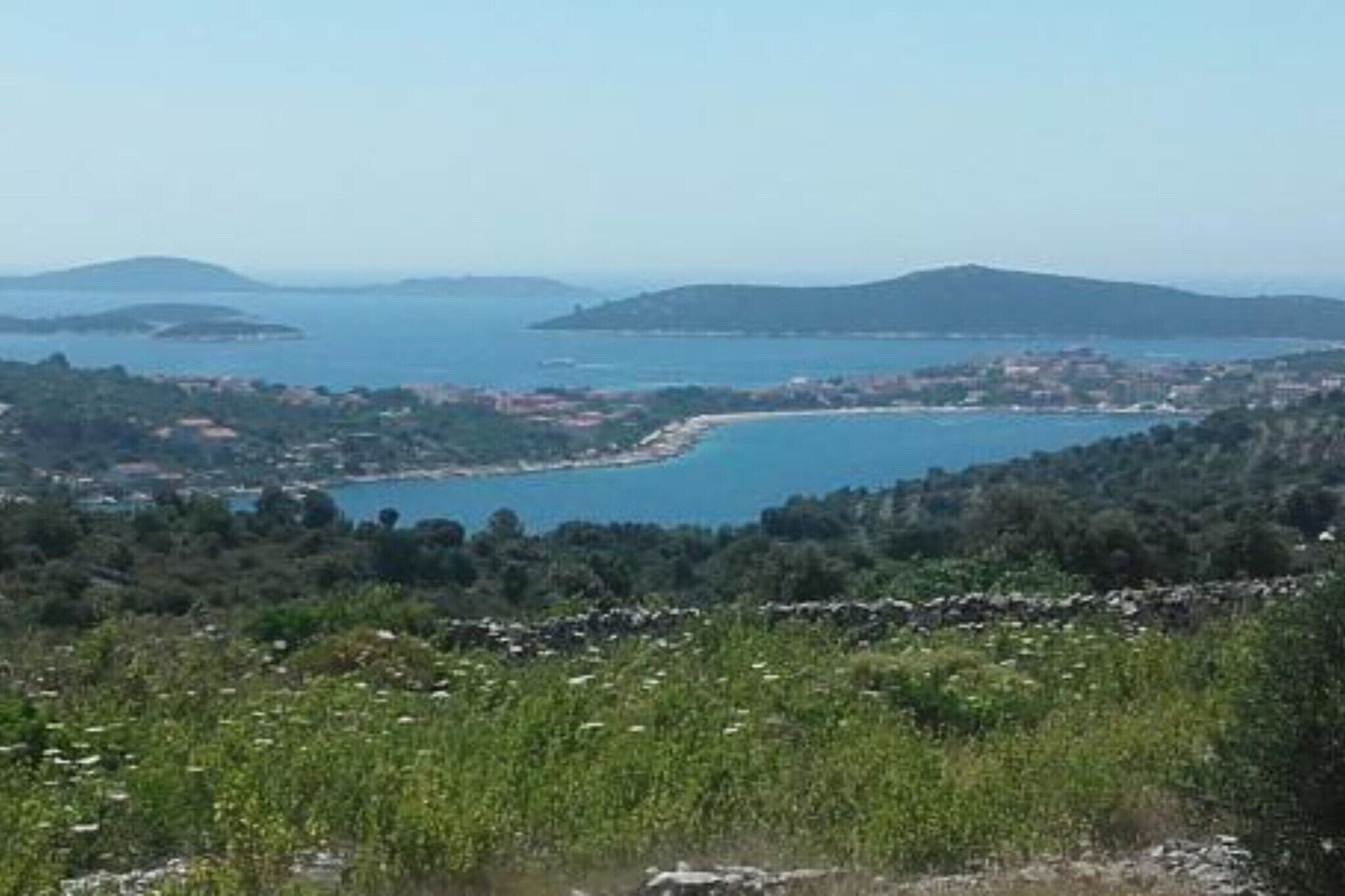 A coastal landscape with a clear view of a bay, surrounded by hills and greenery.