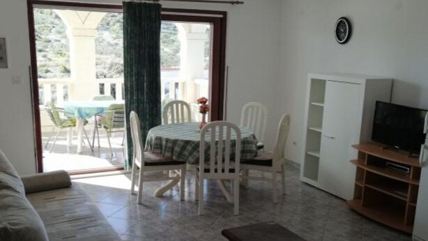 A living room with a sofa, a dining table with chairs, a TV stand, and a sliding glass door leading to an outdoor area with a table and chairs. - Apartments Milakovic-Kanica - One Bedroom Apartment with Sea View and Terrace (Rogoznica)