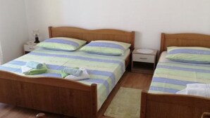 A double room with two wooden beds, each with a striped bedspread and pillows. There is a nightstand with a lamp and a small drawer. - Apartments Milakovic-Kanica - One Bedroom Apartment with Sea View and Terrace (Rogoznica)