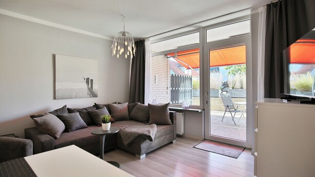 A modern living room with a sectional sofa, a small table with a plant, and a television on a cabinet.