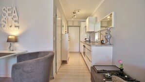 A modern kitchen with white cabinets, a countertop, and a mirror. There is a chair and a table with a lamp.