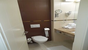 Een kleine badkamer met toilet, handdoekhouder, haardroger en wastafel.