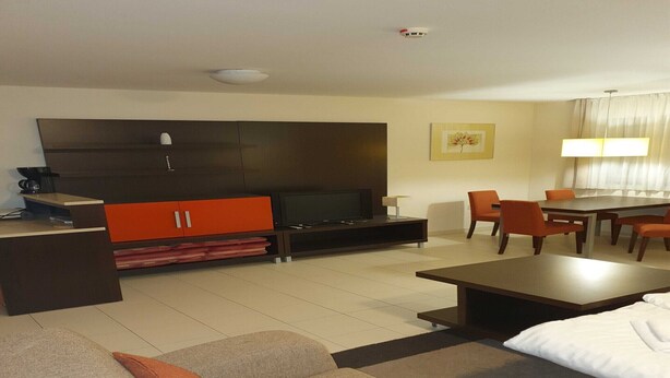 Een moderne hotelkamer met een bank, een salontafel, een televisie, een eettafel met stoelen en een kast.