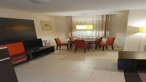 Een moderne woonkamer met een flatscreen televisie, een eettafel met stoelen en een groot raam met gordijnen.