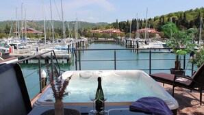 Een jachthaven met aangemeerde boten, een jacuzzi met een fles en glazen, en uitzicht op de omgeving.