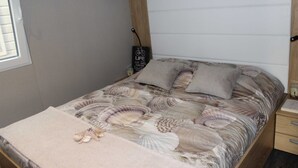 Een bed met een sprei met schelpenprint, een klein nachtkastje met een lamp, en een bordje aan de muur.