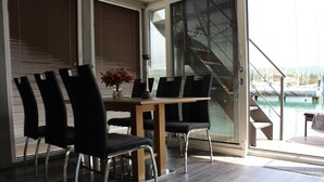Een eethoek met een tafel en stoelen, grote ramen met zonwering, en uitzicht op een zwembad en boten.