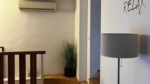 Ett rum med trägolv, en krukväxt, en väggmonterad luftkonditioneringsanläggning och en lampa med en skylt som visar texten "VARVA NER".