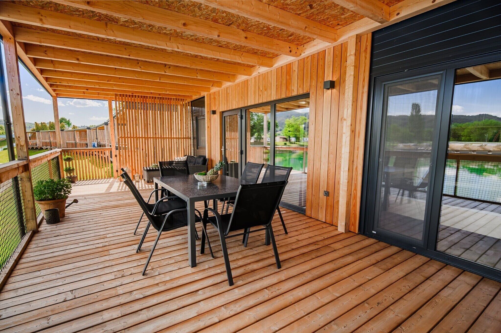 A wooden deck with a table and chairs, a glass door leading to a pool, and a wooden fence in the background.