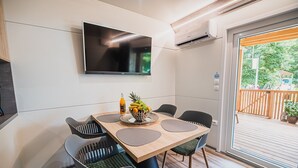 Un espace repas moderne avec une table en bois, des chaises noires et un saladier rempli de fruits. Un téléviseur à écran plat est fixé au mur, au-dessus de la table.