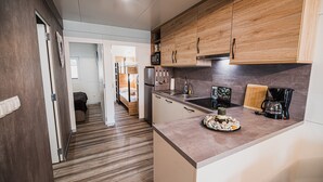 A modern kitchen with wooden cabinets, stainless steel appliances, and a countertop with a coffee maker and a plate of food.