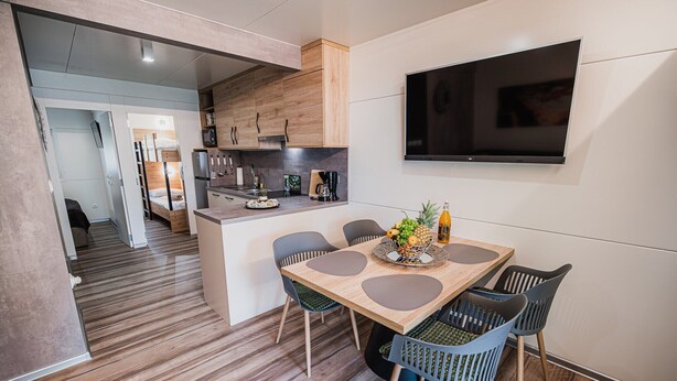 A modern kitchen with wooden cabinets, a built-in oven, and a flat-screen TV mounted on the wall.