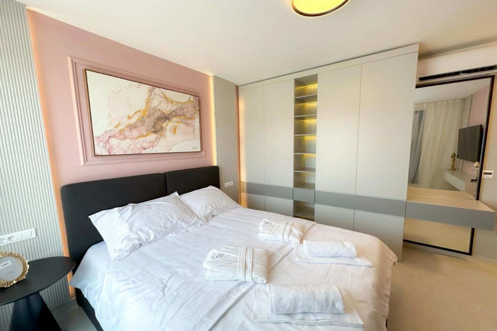 Una habitació d'hotel moderna amb un llit gran, una tauleta de nit, una obra penjada a la paret, un armari i un mirall.