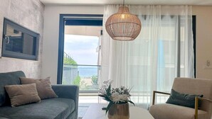 A modern living room with a grey sofa, a beige armchair, a white coffee table, and a large window with a view of greenery and a building.