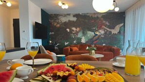 Zona pranzo con un piatto di frutta, succo d'arancia e un televisore montato a parete.