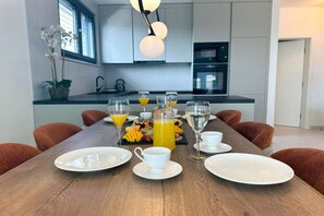 A modern dining area with a wooden table set for breakfast, featuring plates, cups, and a fruit platter.