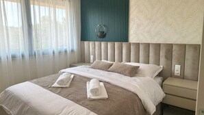 Una camera d'albergo con un letto grande, una testiera, un comodino e una finestra con tende leggere.