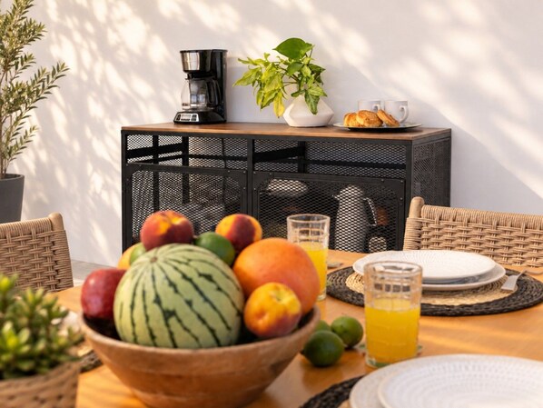 Een ontbijtsetting met een fruitschaal, koffiezetapparaat en ontbijtartikelen op een tafel.