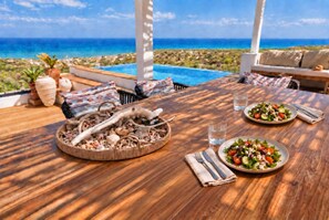 A wooden dining table with a seafood centerpiece, two plates of salad, and a view of the ocean.