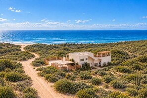 Een modern huis met een plat dak, omgeven door een woestijnlandschap en met uitzicht op een strand.