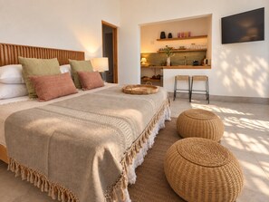 Un dormitorio moderno con cama, mesitas de noche, televisor y una pequeña cocina.