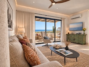 A modern living room with a sofa, armchairs, a coffee table, and a view of the ocean.