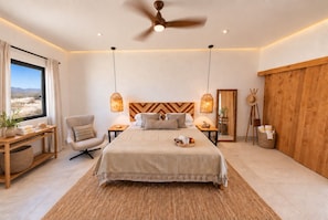 A bedroom with a bed, bedside tables, a chair, a desk, a large window, and a ceiling fan.