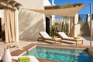 A pool area with two lounge chairs, a small pool, and a staircase leading to an upper level.