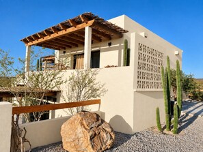 Een modern gebouw met een houten pergola, cactussen en een rots.