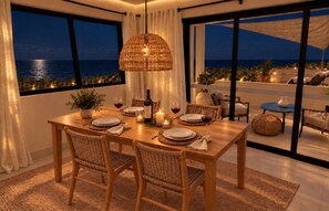 Un coin repas avec une table dressée pour quatre personnes, un luminaire suspendu et une vue sur la mer grâce à de grandes fenêtres.