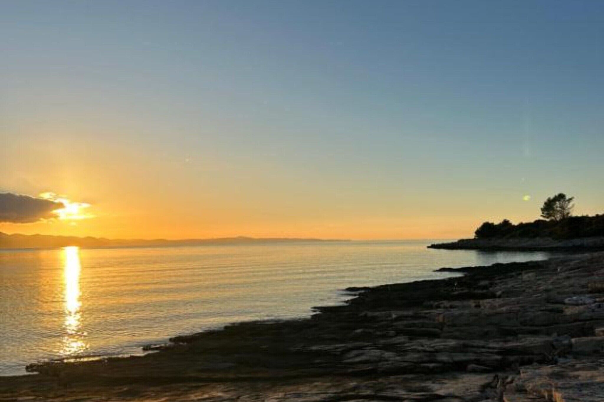 Un coucher de soleil sur une côte rocheuse, les eaux calmes reflétant la lumière du soleil.