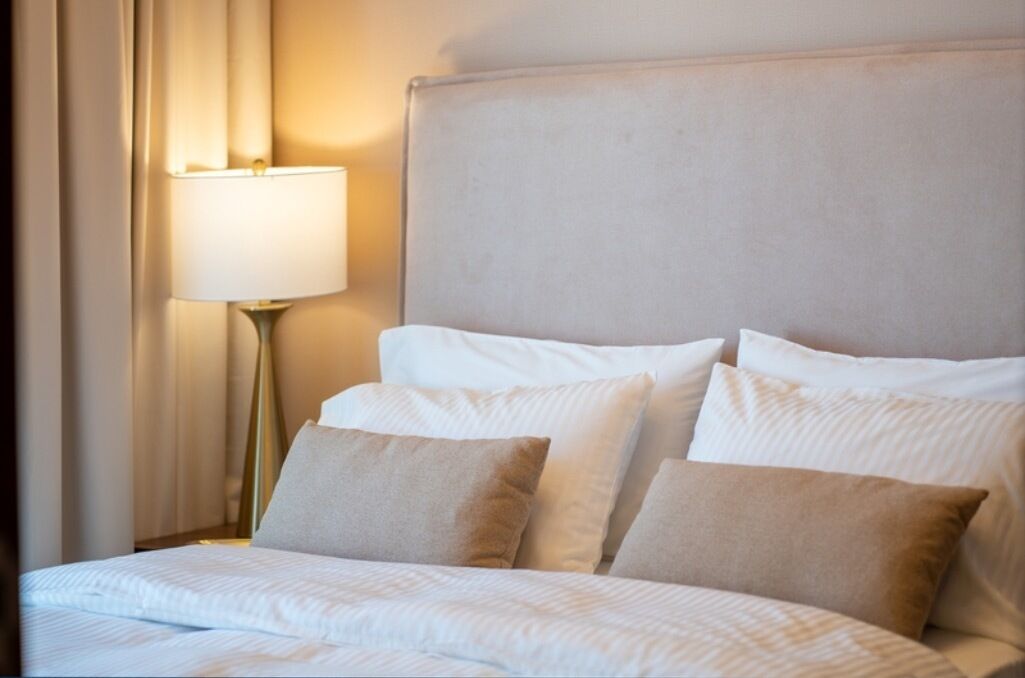 Un lit bien fait, avec du linge de lit blanc et des oreillers beige, une lampe de chevet et une tête de lit.
