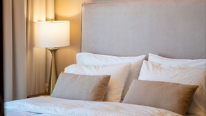 Un letto rifatto con lenzuola bianche e cuscini color beige, una lampada da comodino e una testiera.