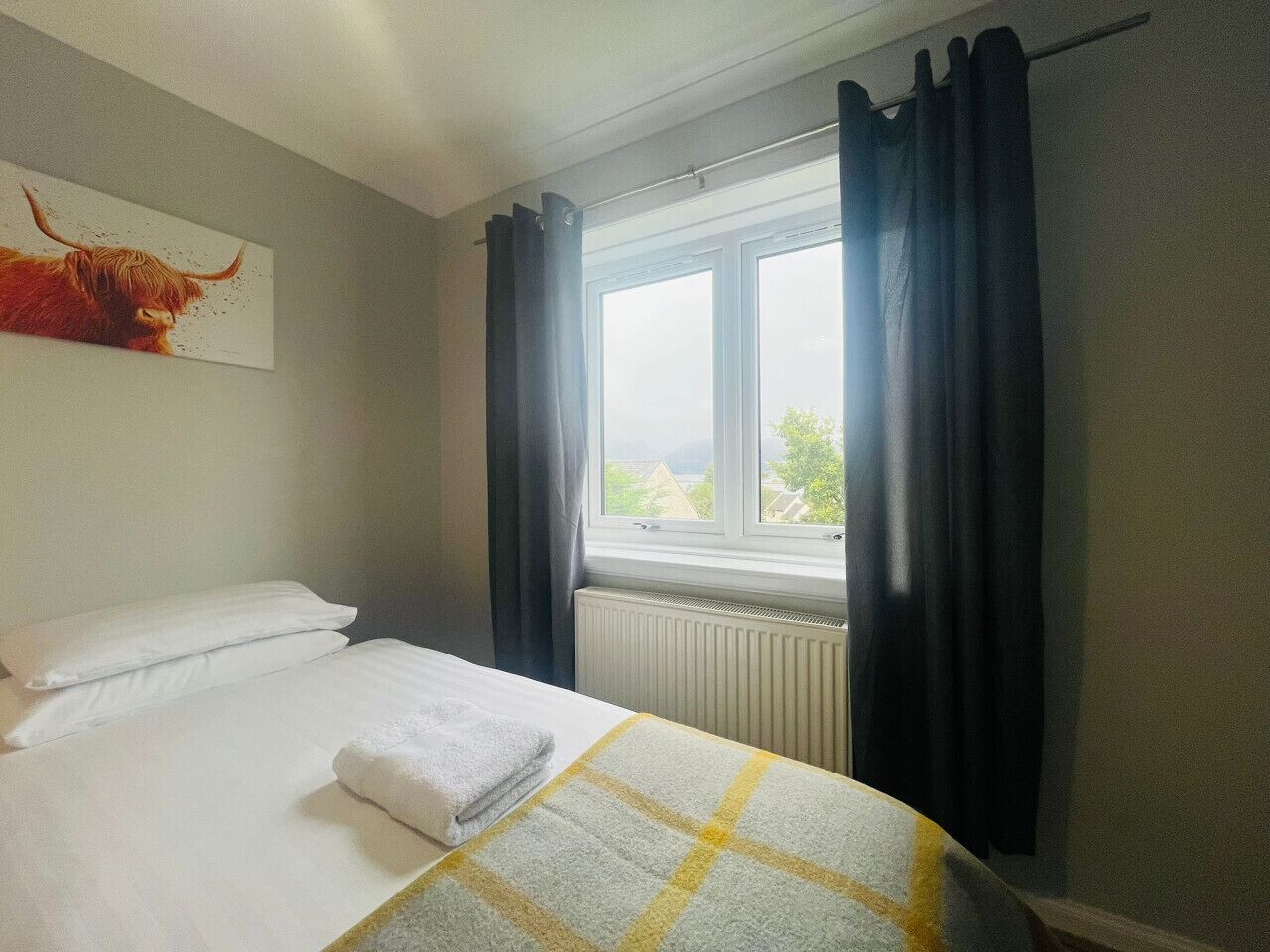Ein Hotelzimmer mit einem Bett, einem Fenster mit Vorhängen, einem Heizkörper und einem Gemälde eines Stiers an der Wand.