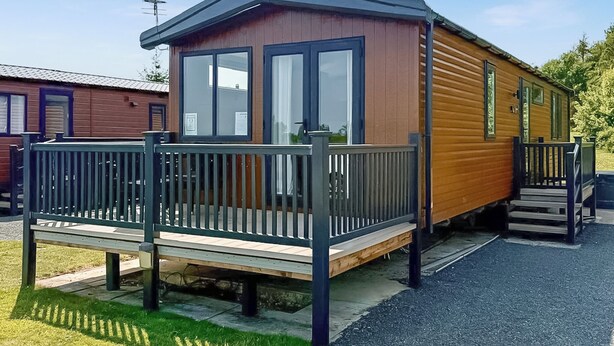 Une maison mobile dotée d’une terrasse, de grandes fenêtres et d’un petit porche.