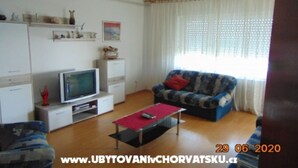 A living room with a television, sofa, and coffee table. There are shelves with decorative items and a window with curtains. - Three-Bedroom Apartment (Seget Donji)