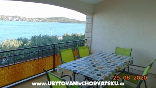 A balcony with a table and chairs, overlooking a body of water and greenery. - Three-Bedroom Apartment (Seget Donji)