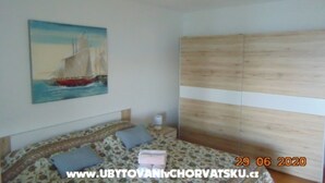 A bedroom with a bed, a bedside table, a nightstand, a painting of a sailboat, and a wooden wardrobe. - Three-Bedroom Apartment (Seget Donji)