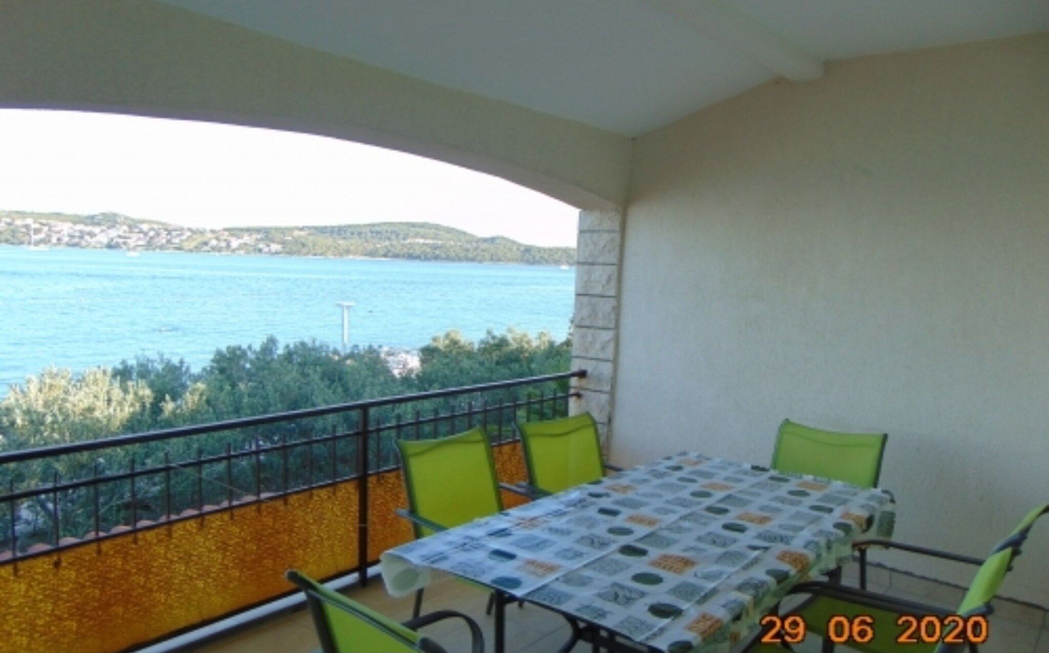 A balcony with a table and chairs, overlooking a body of water and greenery.