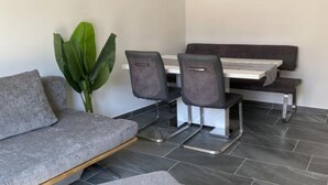 A modern room with a grey sofa, a dining table with four chairs, a bench, and a large green plant. - Apartments Stone House Murter - Two Bedroom Apartment (Murter)