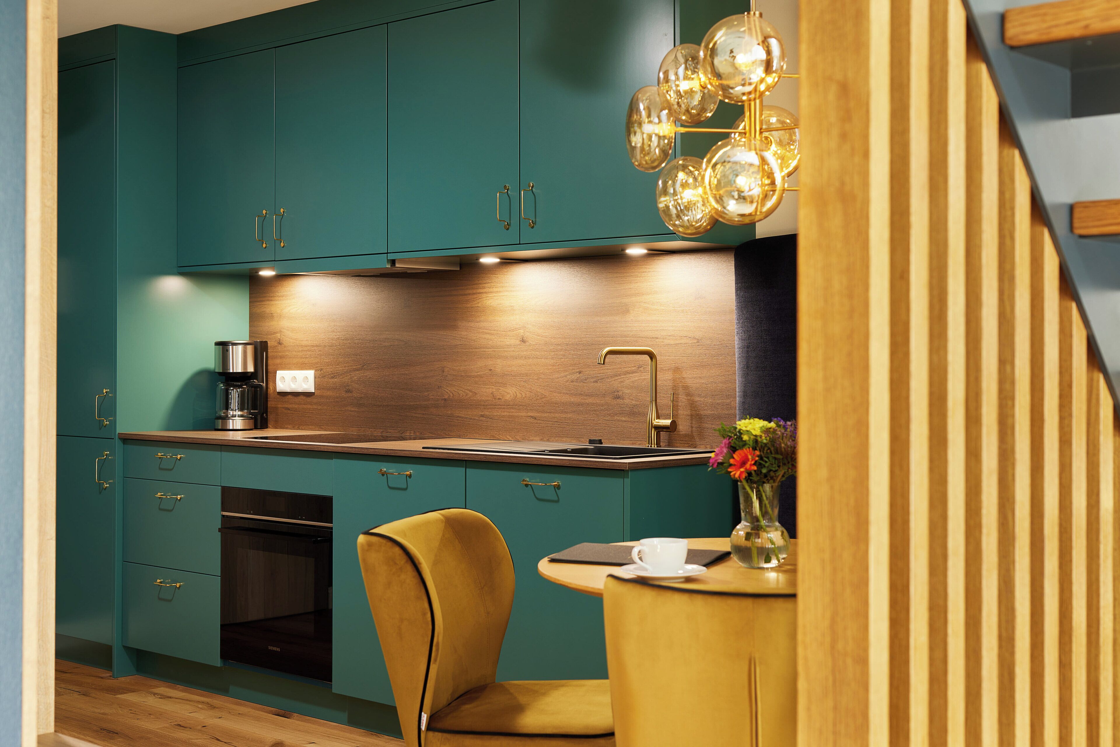 A kitchen with teal cabinets, a wooden countertop, a coffee maker, and a yellow chair.