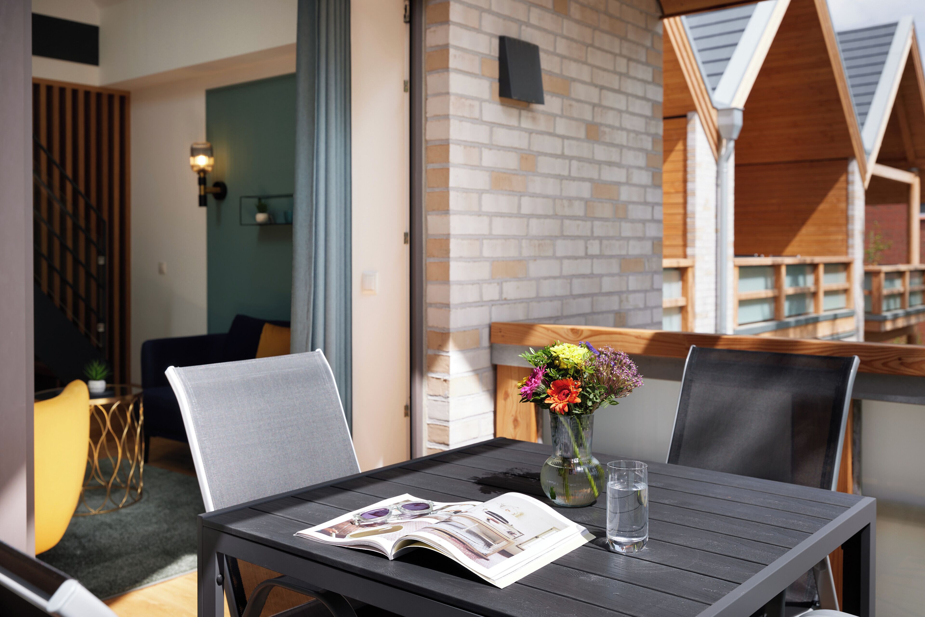 A dining table with a magazine, a glass of water, and a vase with flowers.