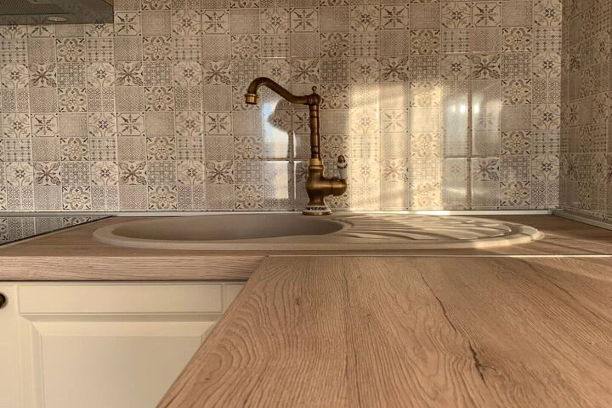 Una cocina con encimera de madera, un lavamanos con grifo antiguo y azulejos decorativos en la salpicadera.