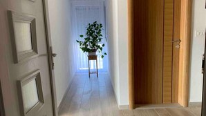 Een gang met een houten deur, een potplant en een witte deur aan het einde.