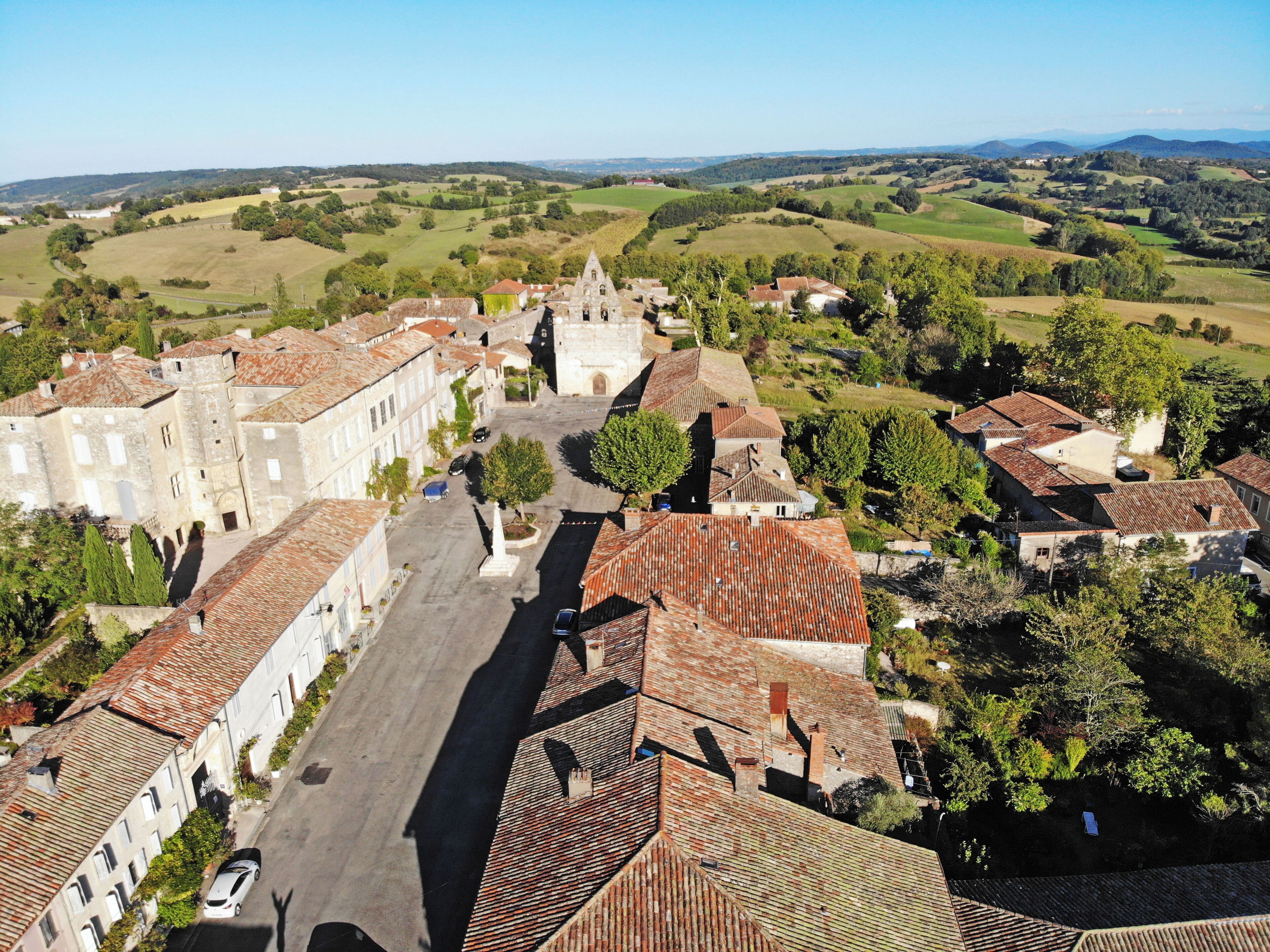 An aerial view of a historic town with traditional architecture, a central square, and surrounding green fields.