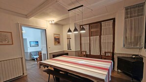 Ruokailutila, jossa on pitkä pöytä, penkit, riippuvalaisimet ja piano.