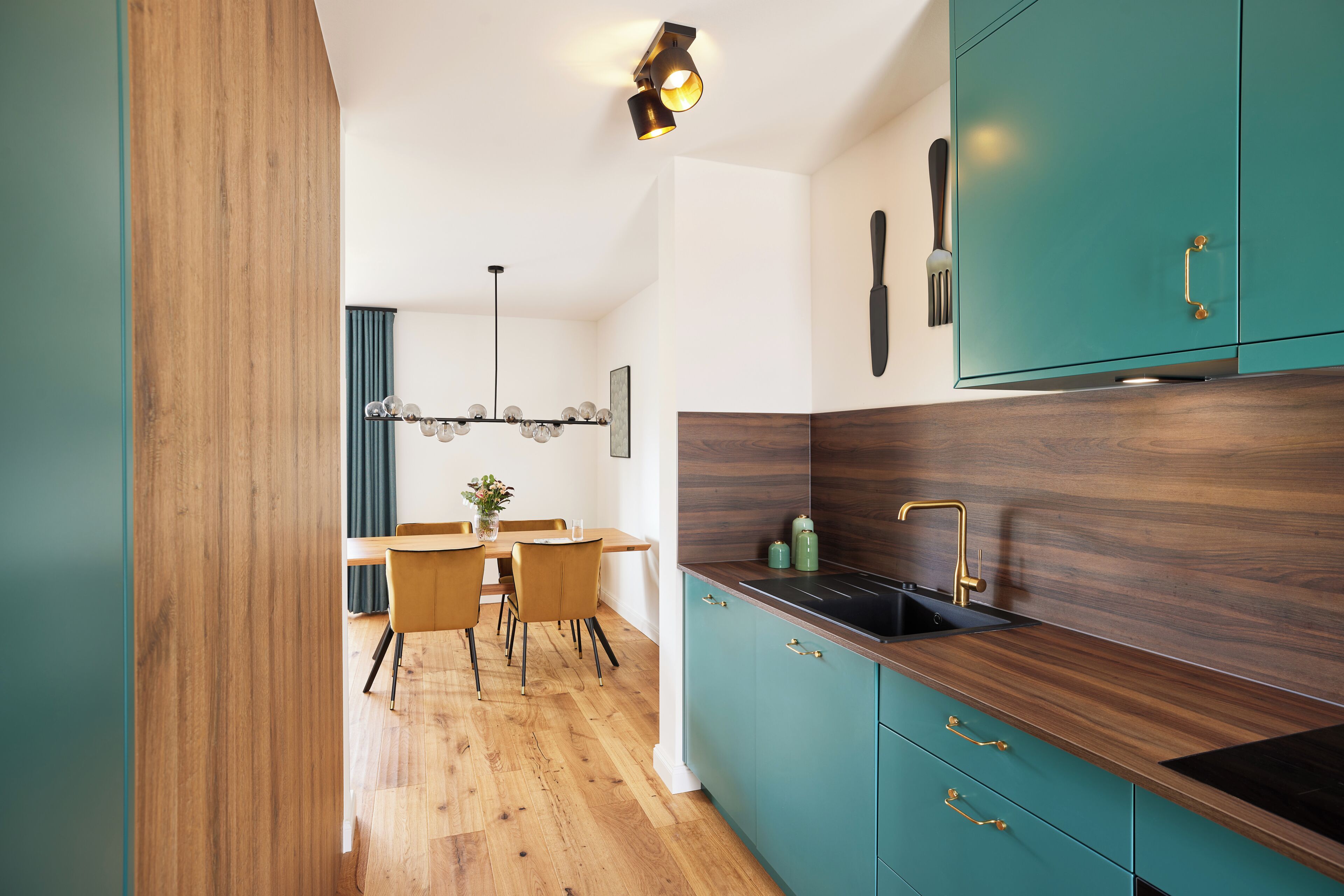 A modern kitchen with teal cabinetry, a wooden countertop, and a black sink.
